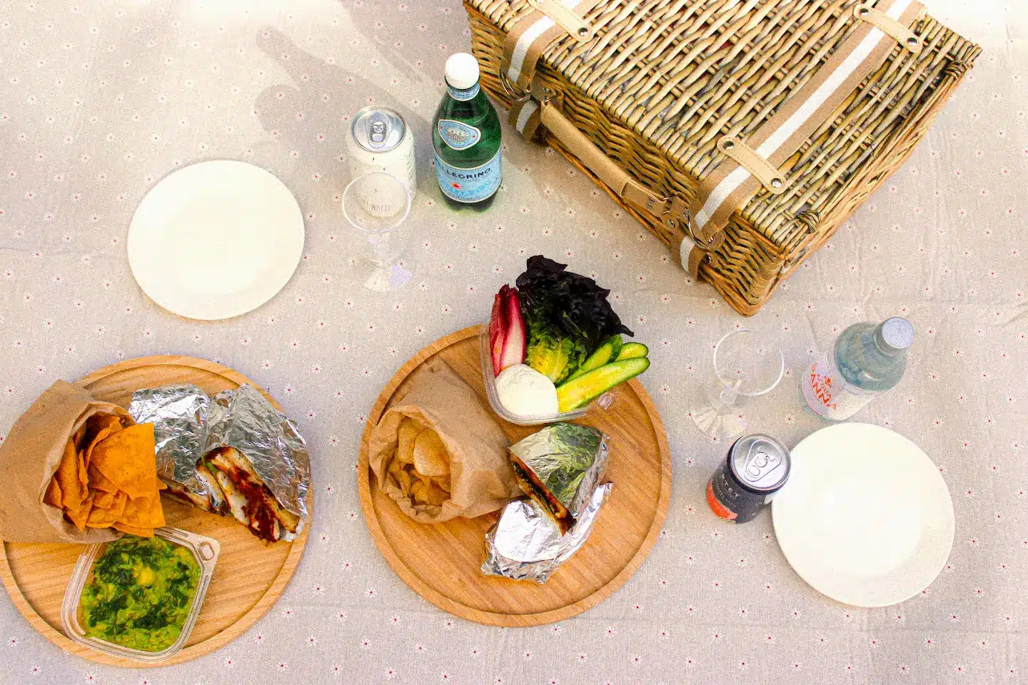 a picnic setup with plates, food, drinks, and a wicker basket