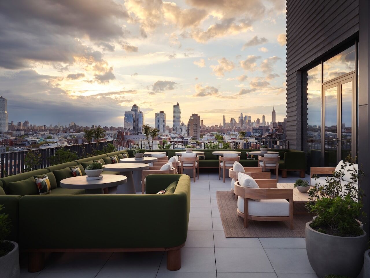 A rooftop terrace with outdoor seating and a city skyline view at sunset.